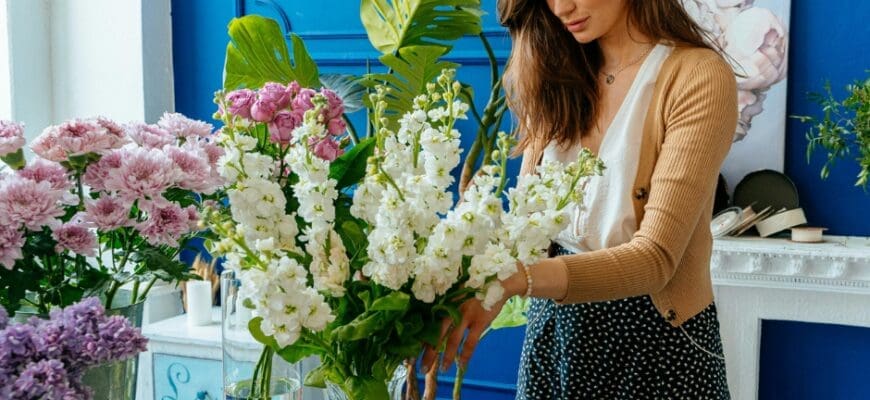 A Woman Arranges Flowers in a Large Vase on Top of a Table